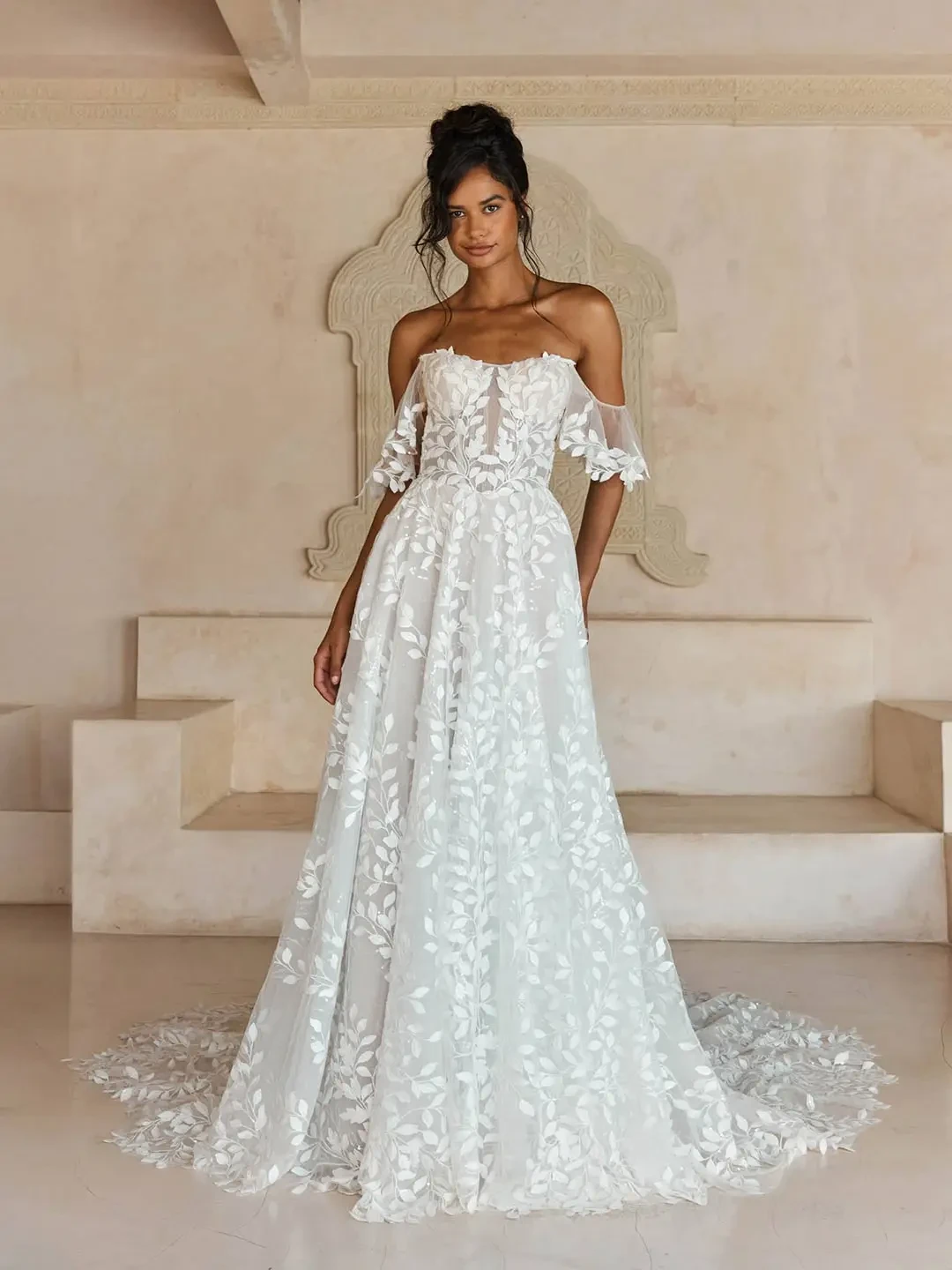 Model is wearing an A-line gown with glitter tulle and sequin leaf lace, featuring a peak neckline and detachable straps and sleeves.