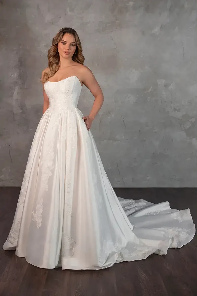 Model is wearing a strapless Mikado ballgown with a scooped cat-eye neckline, Basque waist, and voluminous pleated skirt.