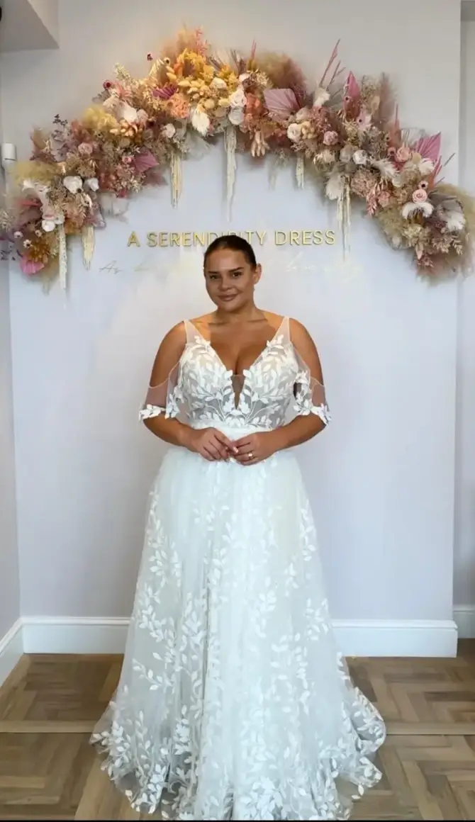 A woman in a white wedding dress stands in front of a floral backdrop with the words 